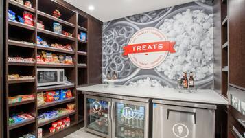 Una sección bien organizada de aperitivos y artículos de conveniencia, con una variedad de alimentos y bebidas envasadas, un microondas y un refrigerador.