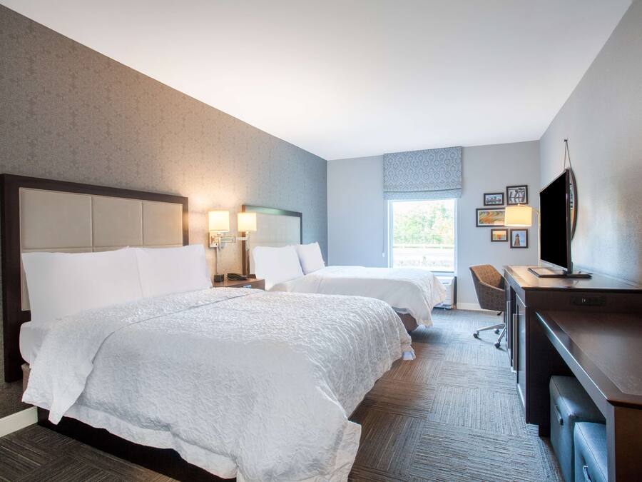 A hotel room with two beds, a desk, a chair, and a TV.