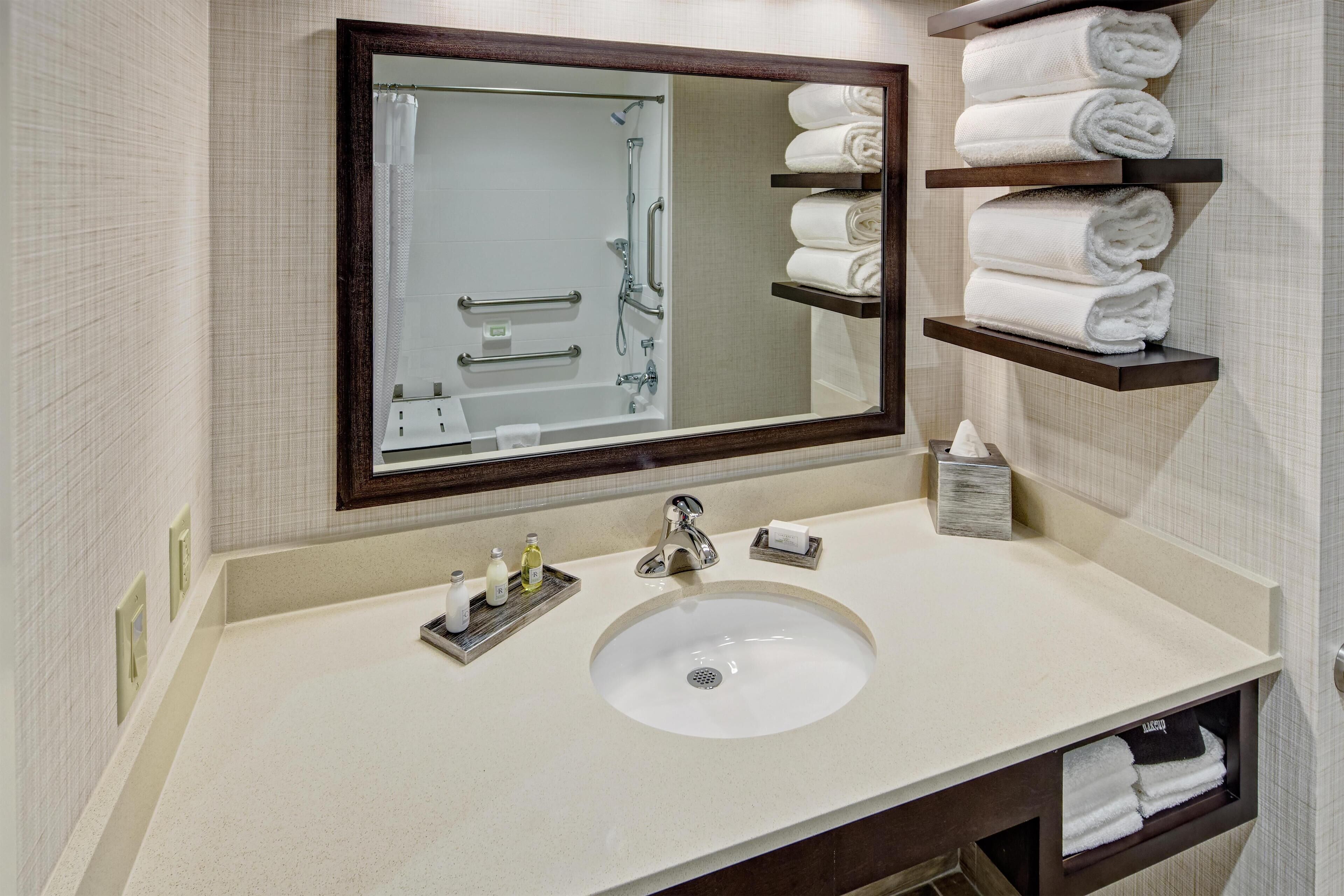 A bathroom with a large mirror, a sink, and shelves with folded towels.
