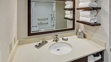 A bathroom with a large mirror, a sink, and shelves with folded towels.