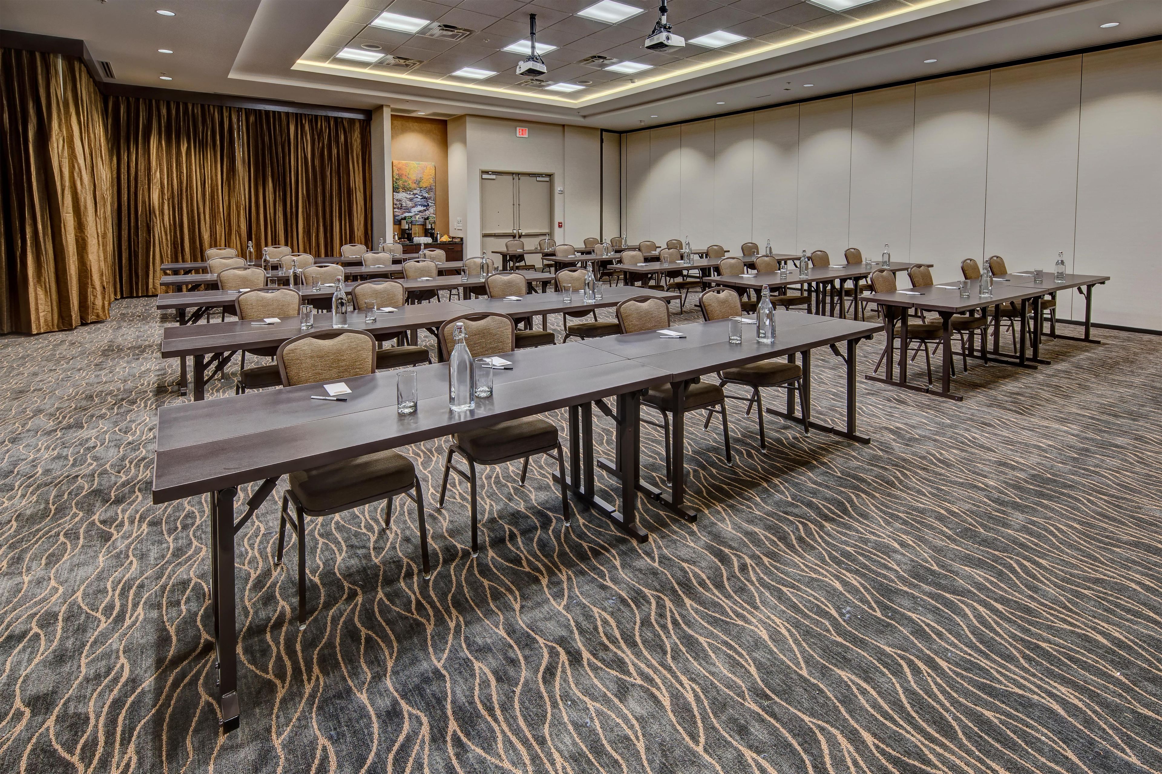 A conference room with multiple tables and chairs, a carpeted floor, and a door with an exit sign.