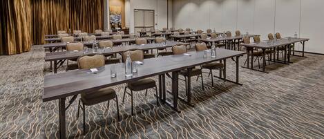A conference room with multiple tables and chairs, a carpeted floor, and a door with an exit sign.