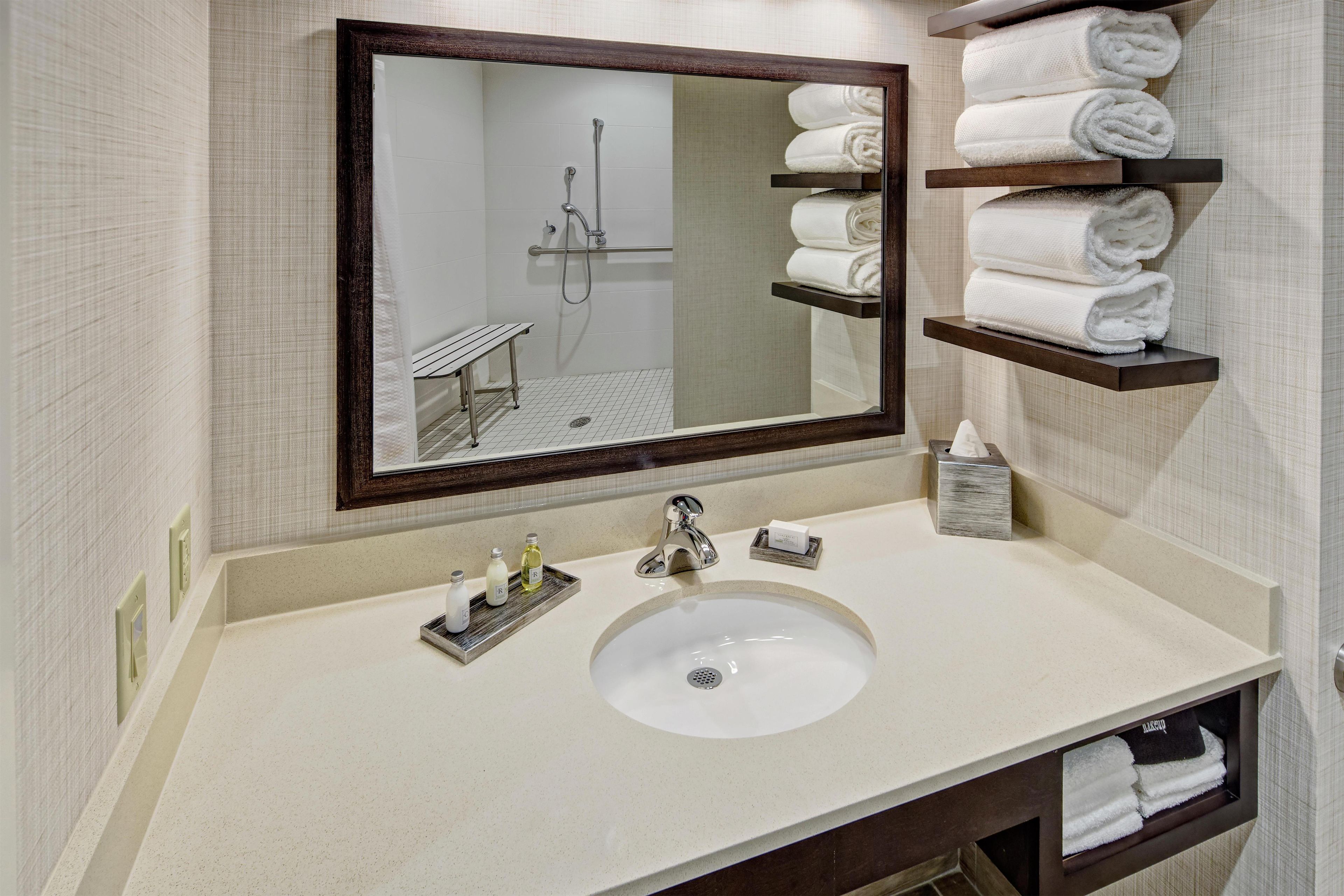 A bathroom with a large mirror, a sink, and shelves holding folded towels.