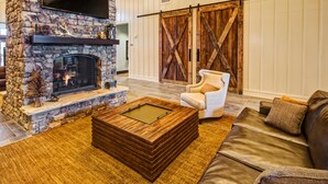 Un salon chaleureux avec une cheminée en pierre, une grande table basse en bois, un canapé en cuir et une porte coulissante de style rustique.