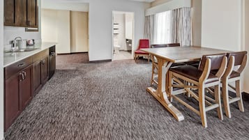 Habitación de hotel con cocina, una mesa de comedor y sillas, y vista al pasillo.