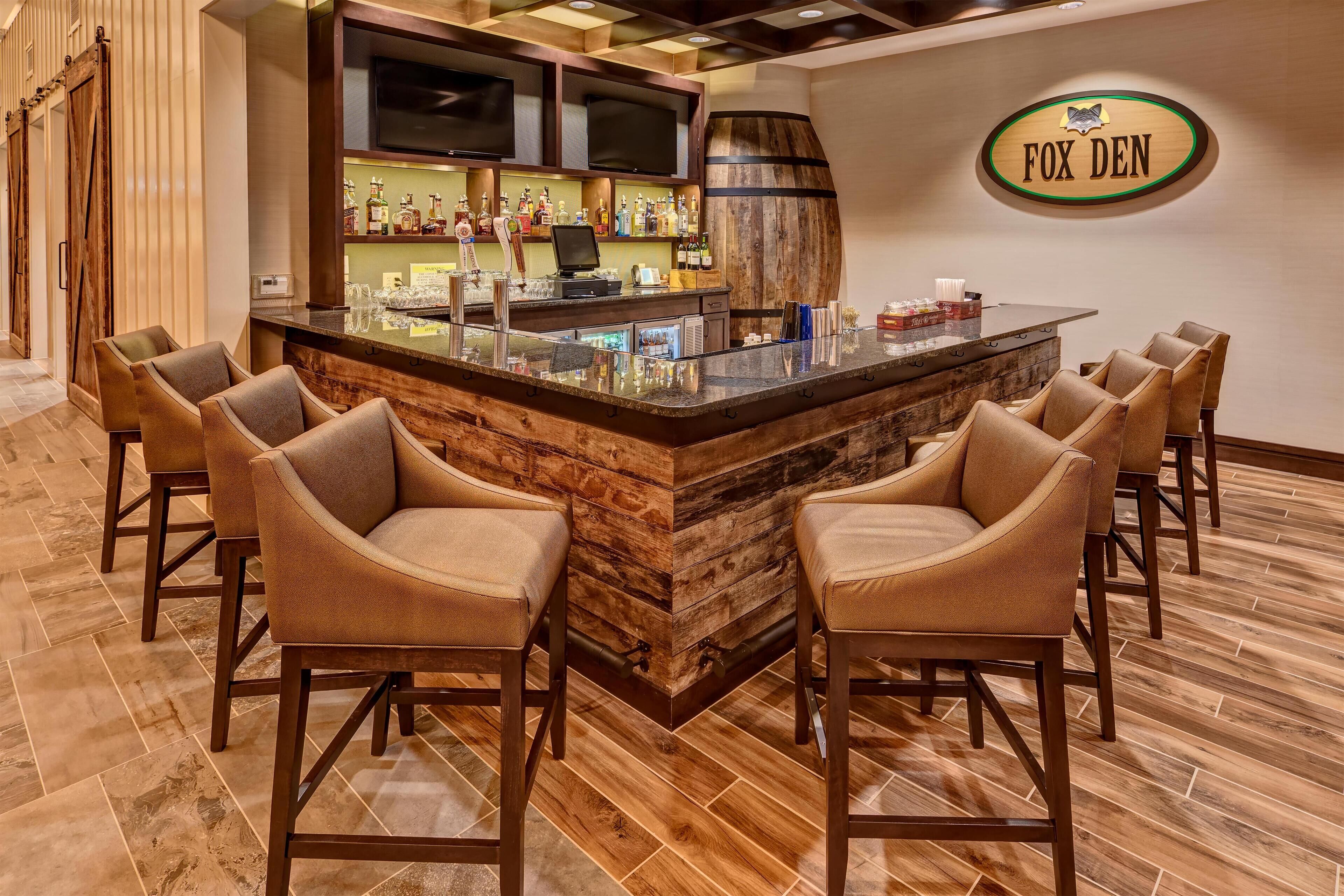 A bar area with a wooden bar counter, multiple bar stools, and a television mounted above the bar.