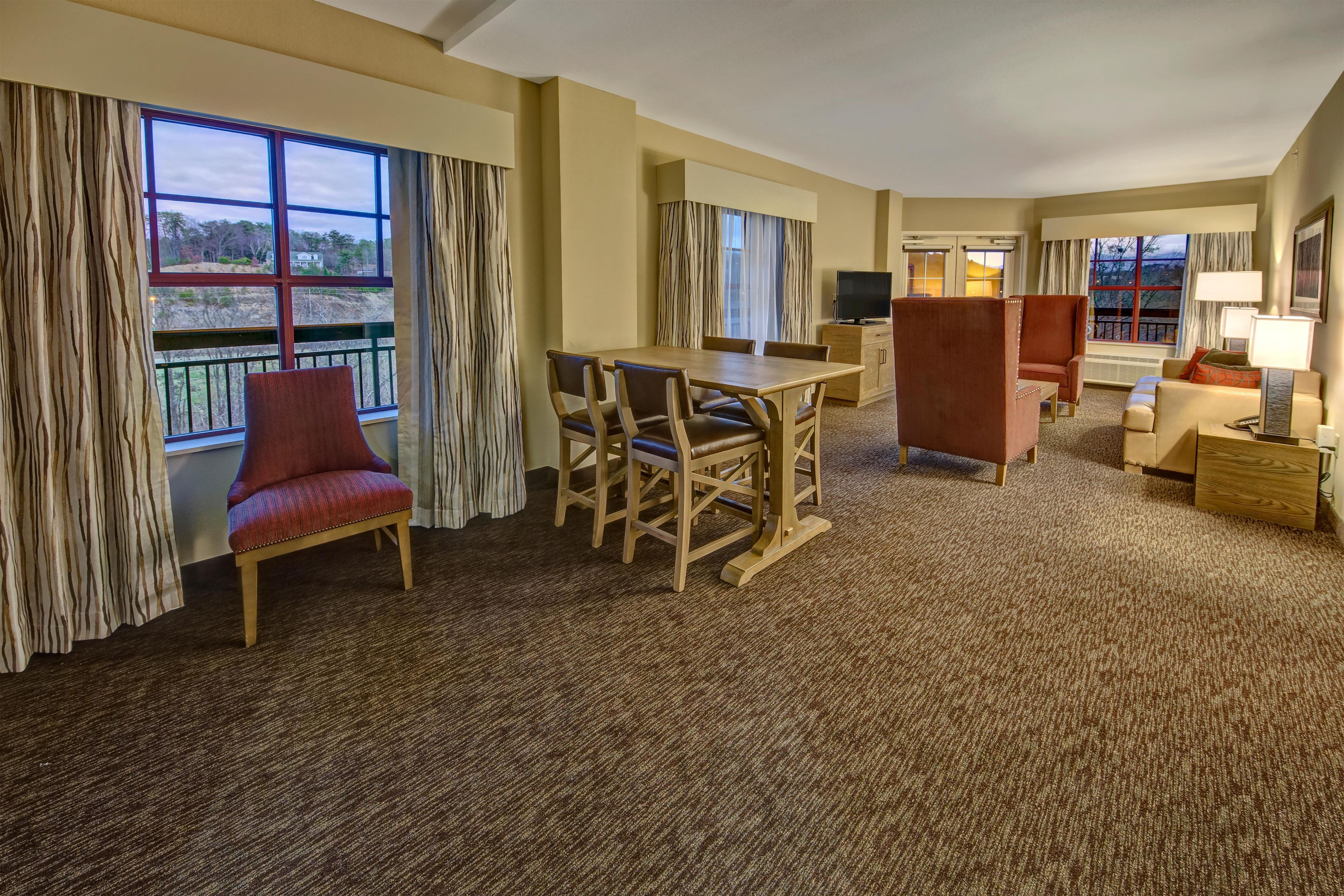 A hotel room with a dining area, a red armchair, a wooden table, and a sofa.