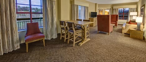 A hotel room with a dining area, a red armchair, a wooden table, and a sofa.