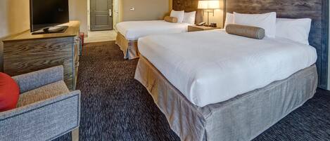 Ein Hotelzimmer mit zwei Betten, einem Fernseher, einem Schreibtisch und einem Sessel.