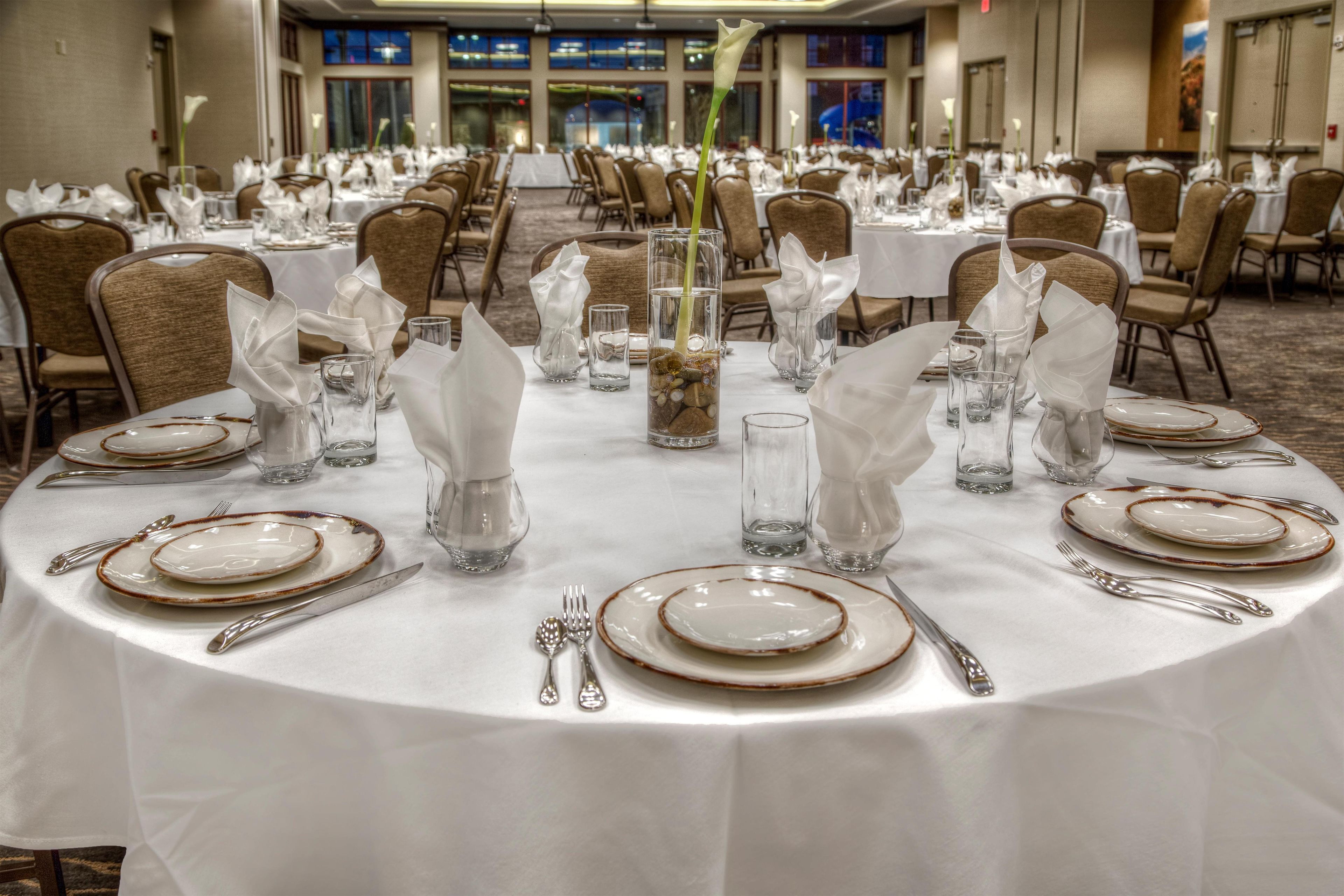 Un salón de banquetes con mesas redondas dispuestas para comer, con platos, cubiertos y copas.