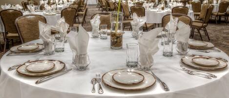 Un salón de banquetes con mesas redondas dispuestas para comer, con platos, cubiertos y copas.