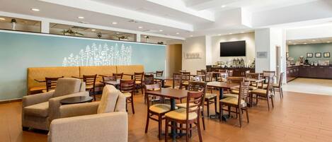 A spacious lobby with multiple seating areas, including sofas and tables, and a large television screen on the wall.