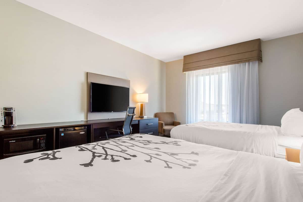 Habitación de hotel con una cama grande, un escritorio, un televisor de pantalla plana, una silla, una lámpara y una ventana con cortinas.