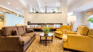 A modern lobby with a brown sofa, yellow armchairs, a patterned carpet, and a decorative plant centerpiece. - Sleep Inn & Suites Middletown - Goshen (Middletown)