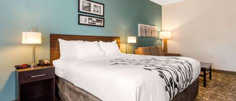 A hotel room with a large bed, two bedside tables with lamps, a small desk, and a wall with framed pictures.