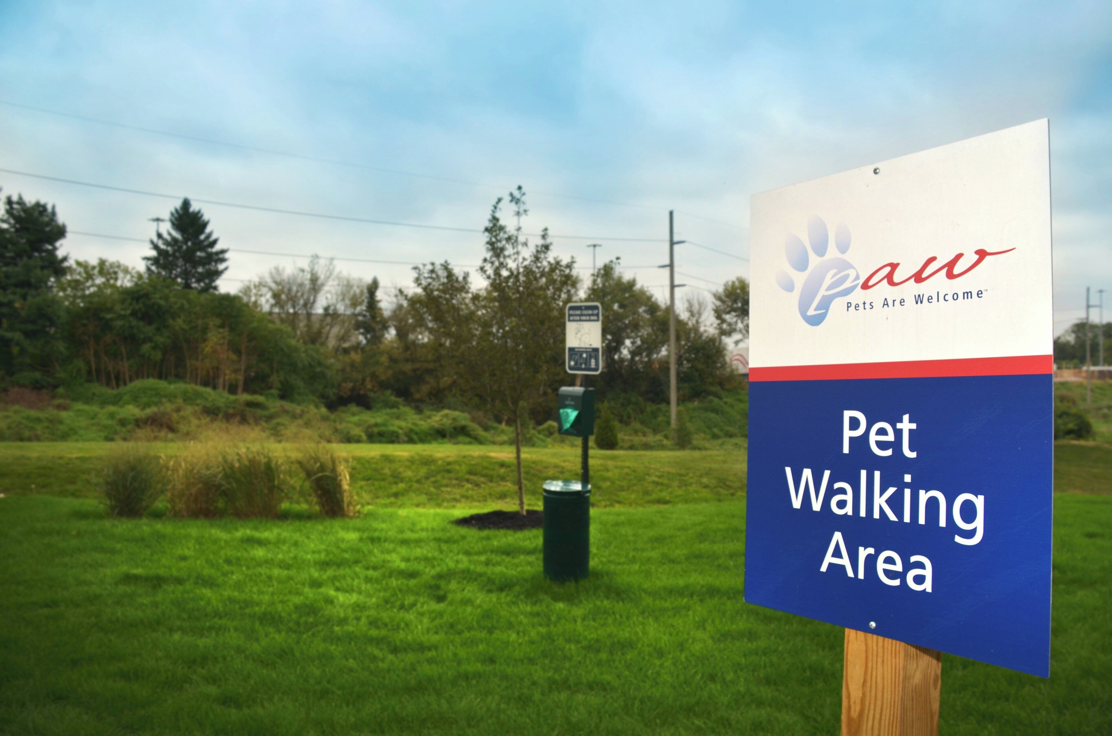 A sign for a Pet Walking Area with a logo for Paw Pets Are Welcome.