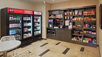 A self-service kiosk area with beverage dispensers, a microwave, and a variety of snacks and groceries.