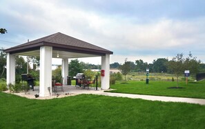 A covered outdoor area with a barbecue grill, chairs, and a trash can. - Candlewood Suites York by IHG (York)