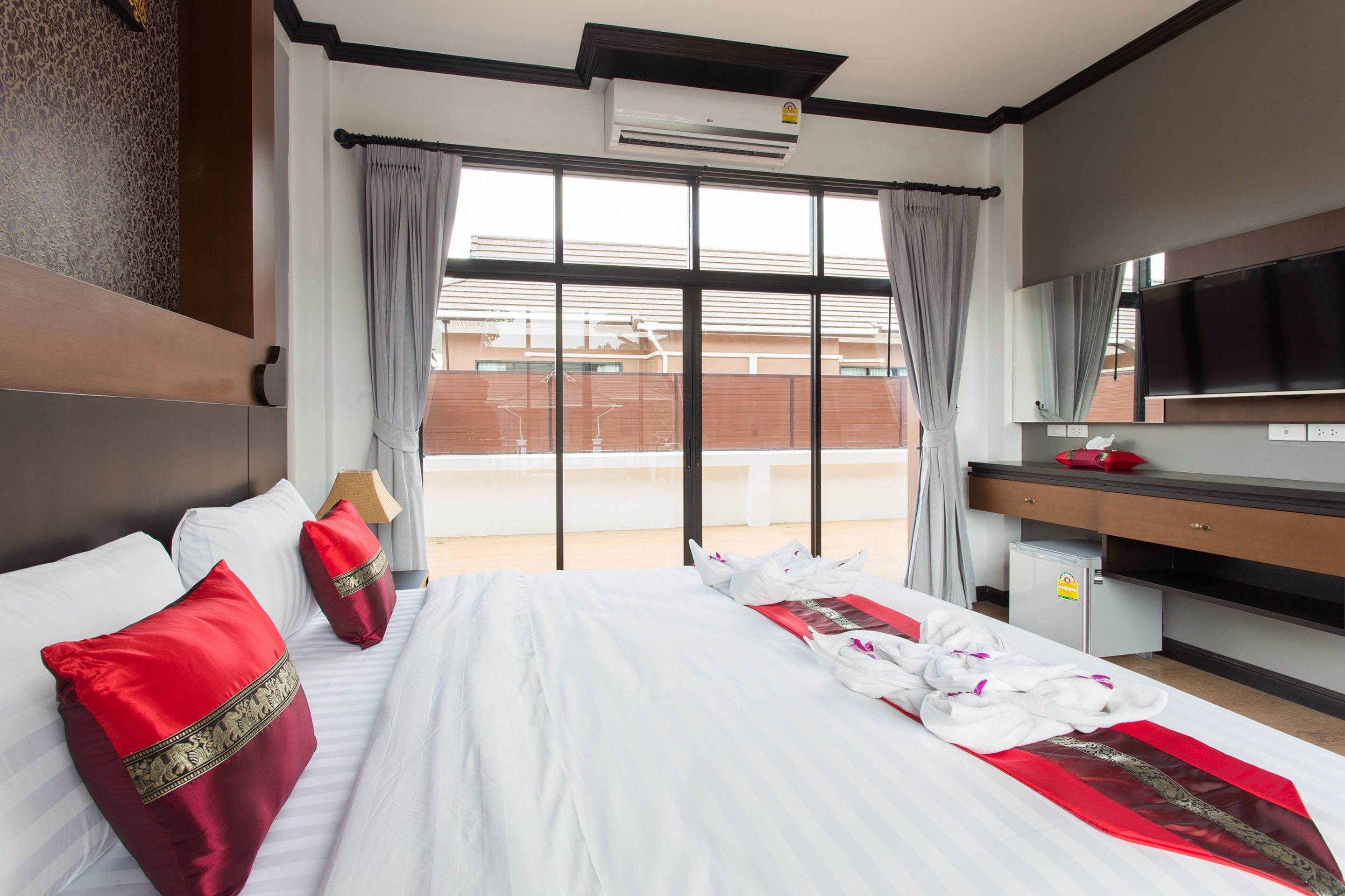 A hotel room with a large bed, a desk, a flat-screen TV, and a window with curtains.