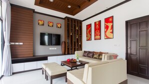 A modern living room with a sofa, coffee table, and TV. There are decorative wall panels and a wooden ceiling. - The Best Aonang Villas (Krabi)
