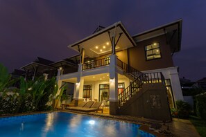 Una casa de dos pisos con piscina, un balcón y una escalera que conduce al piso superior.