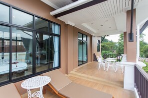 Una habitación de hotel moderna con ventanas amplias, un balcón con mobiliario exterior y suelo de madera.