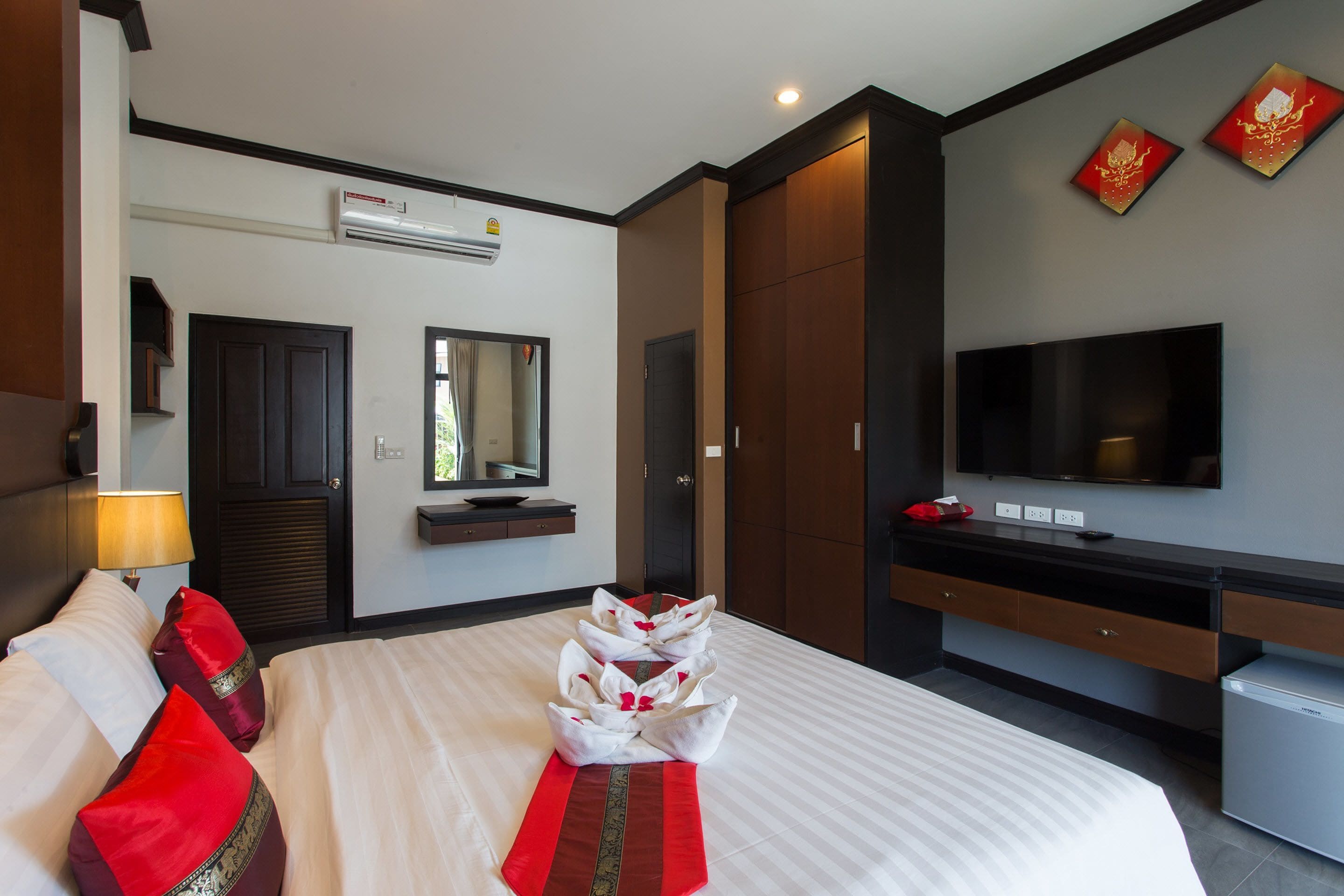A hotel room with a large bed, a TV, a wardrobe, and a desk with a computer.