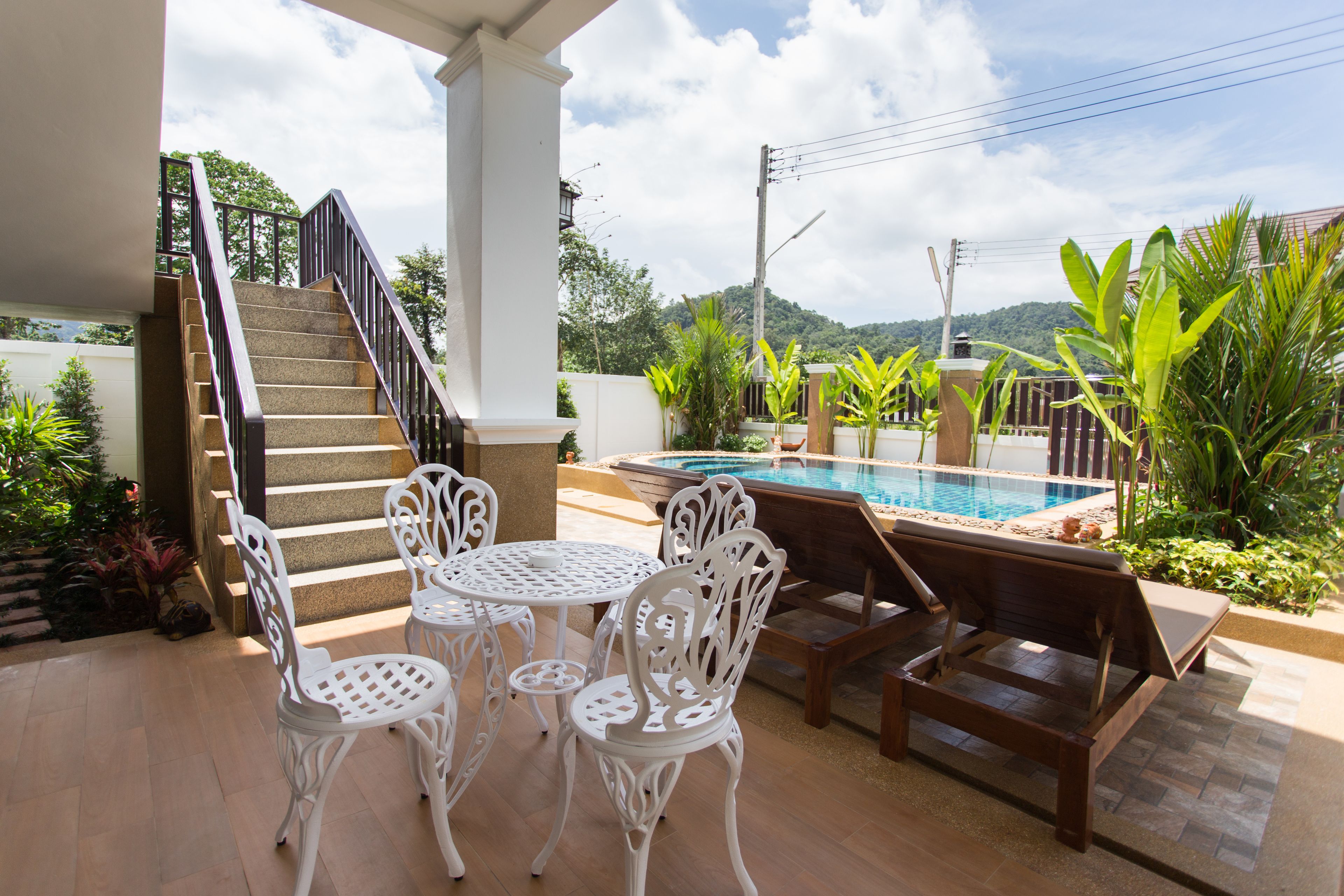 A patio with a pool, white chairs, a wooden bench, and a staircase.