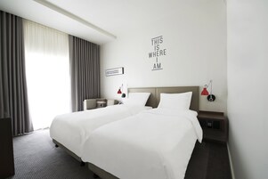 A hotel room with two beds, a desk, a nightstand, a red lamp, and a wall sign.