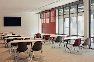 Un aula con mesas y sillas, ventanas amplias y un televisor de pantalla plana en la pared.