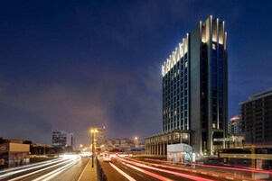A modern hotel with a prominent illuminated sign, a busy street with light trails, and a clear view of the building's facade.