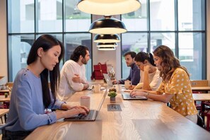 A group of people seated around a wooden table in a modern indoor setting with large windows and pendant lighting. - Rove Bur Dubai Healthcare City (Dubai)