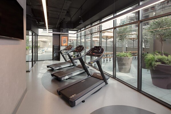 A gym with treadmills, large windows, and a view of the outside. - Rove Bur Dubai Healthcare City (Dubai)