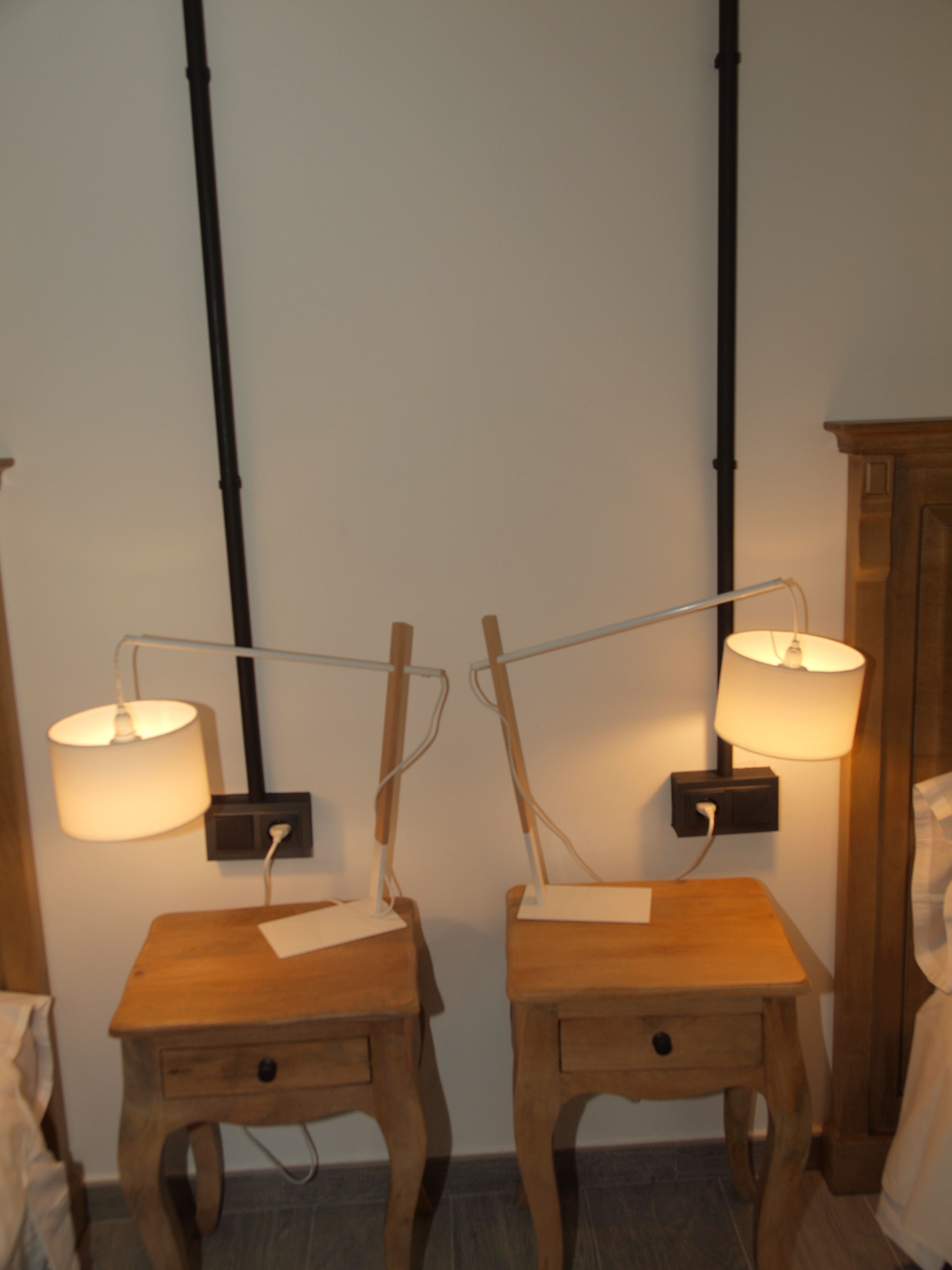 Two wooden nightstands with lamps, a wooden cabinet, and a white wall with a black pipe.
