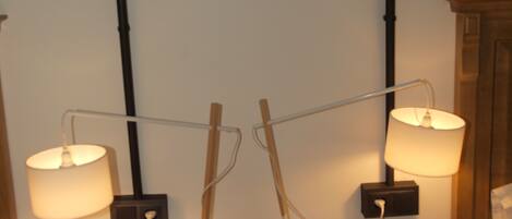 Two wooden nightstands with lamps, a wooden cabinet, and a white wall with a black pipe.