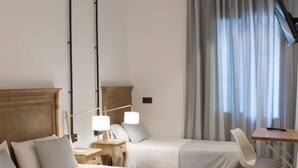 Ein Hotelzimmer mit zwei Betten, einem Schreibtisch mit Stuhl, einer Lampe und einem großen Spiegel.