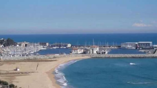 Eine Küstenstadt mit einem Yachthafen, Sandstrand und einem Felssteg.
