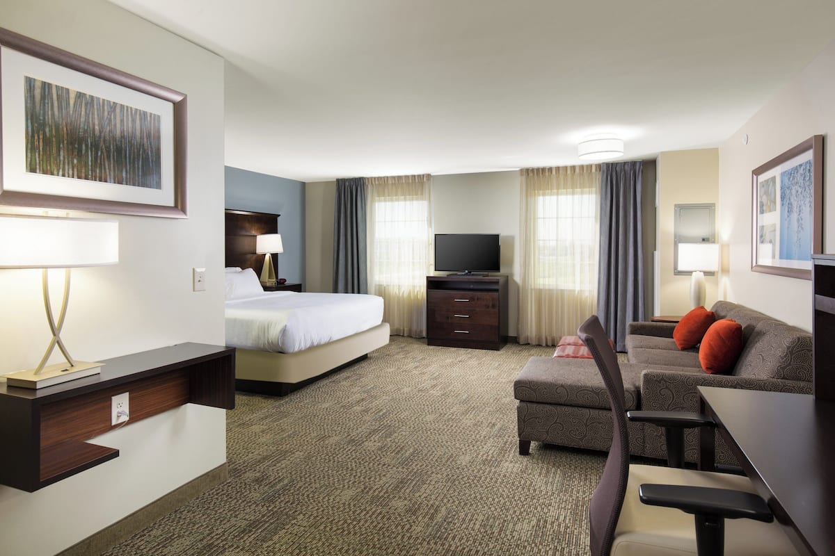 A hotel room with a bed, a desk with a chair, a television, and a sofa with cushions.