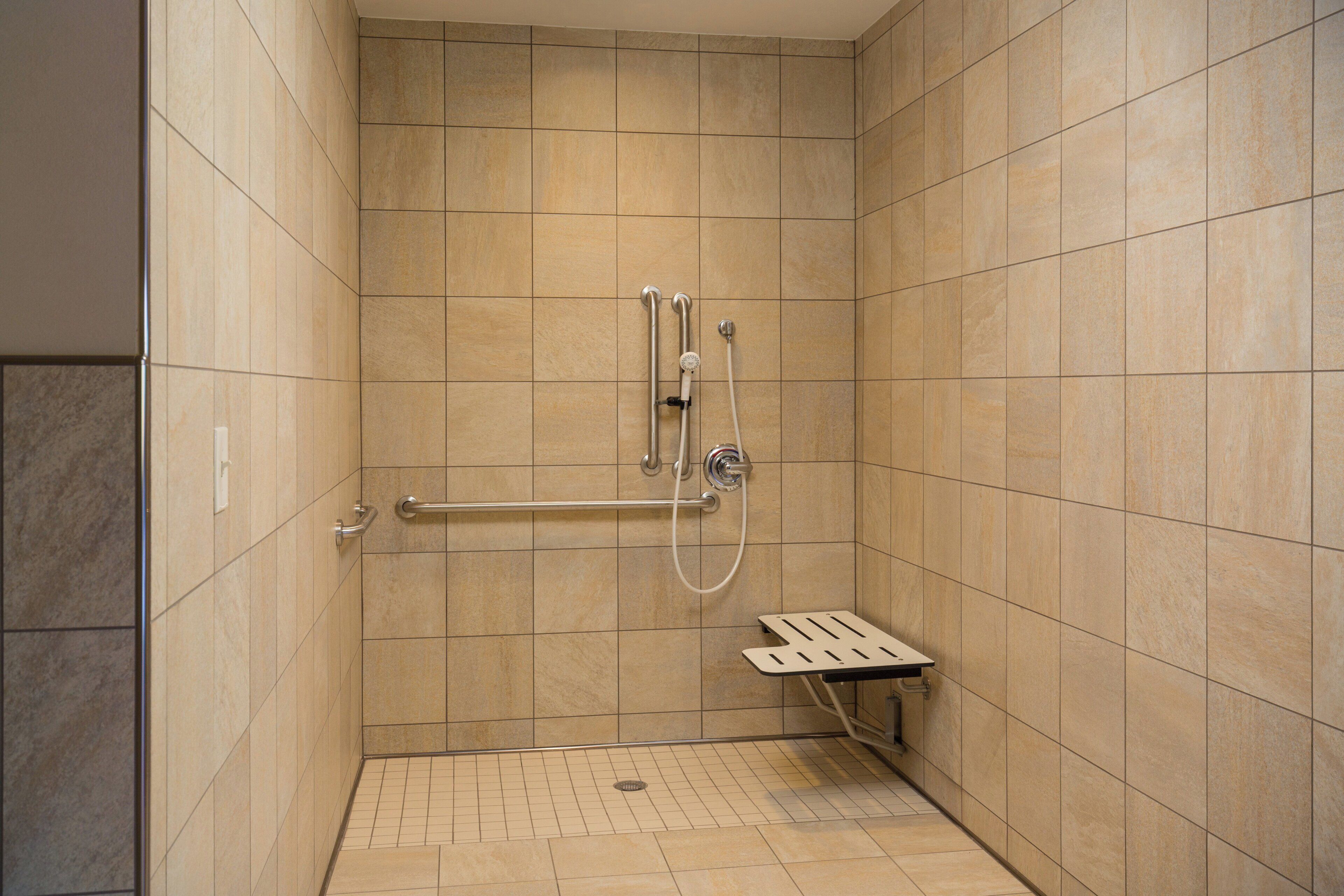 A shower area with a handrail, a handheld showerhead, and a floor drain.