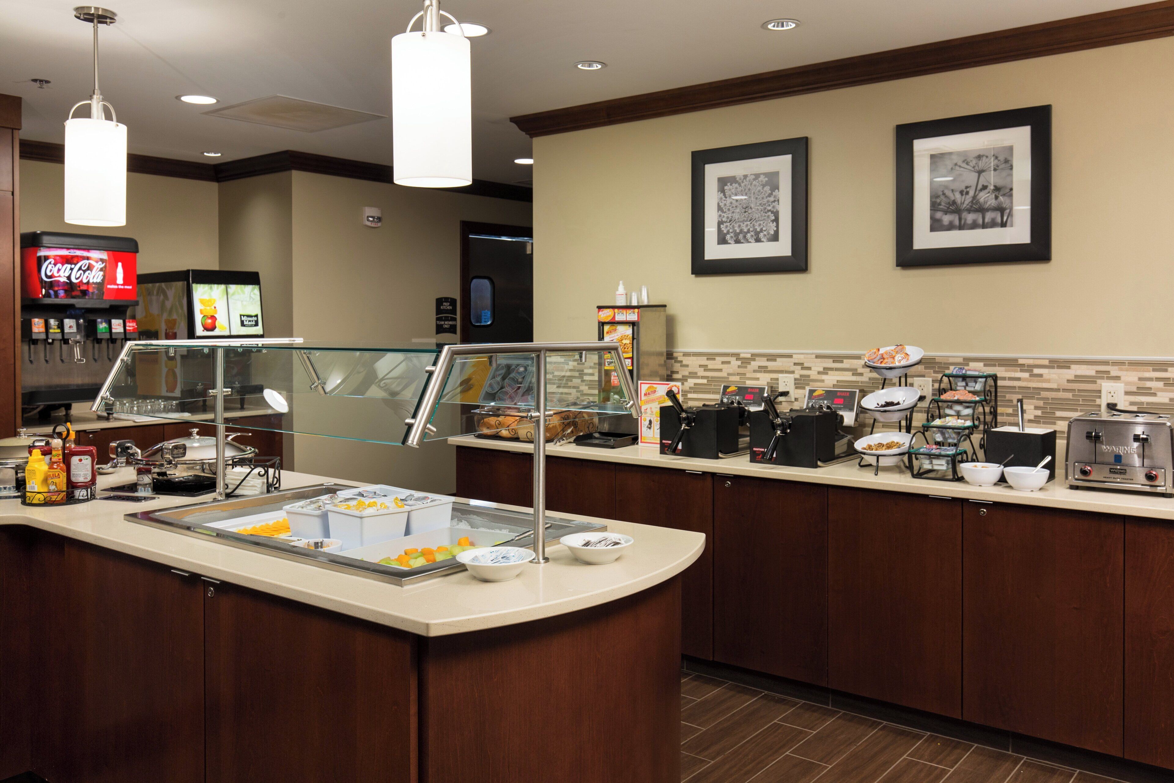 A self-service breakfast area with a Coca-Cola machine, a microwave, and various food items.