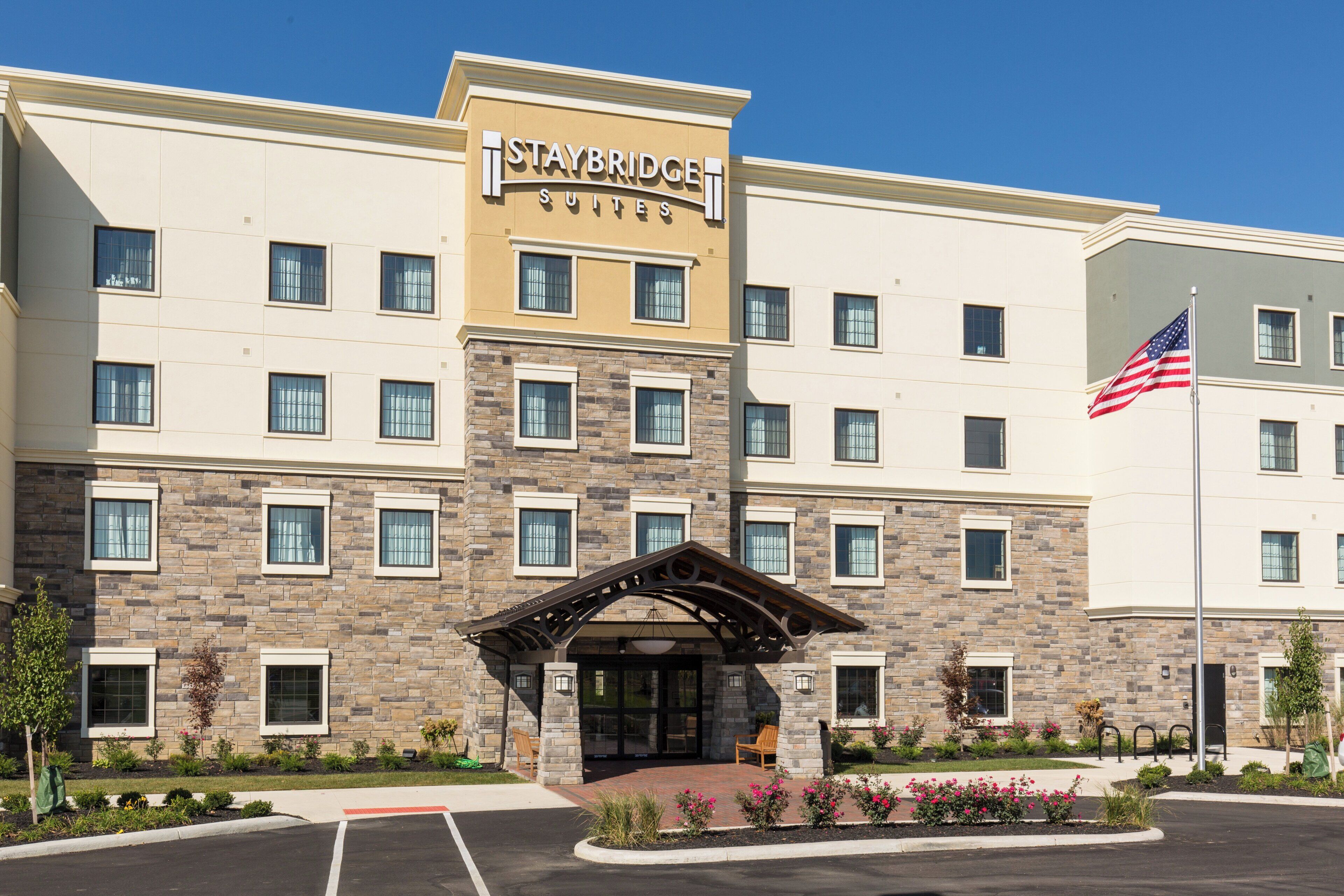 A Staybridge Suites hotel with a stone facade, multiple windows, and an American flag.