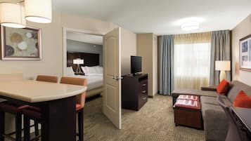 A hotel room with a dining area, a sofa, a TV, and a bed.