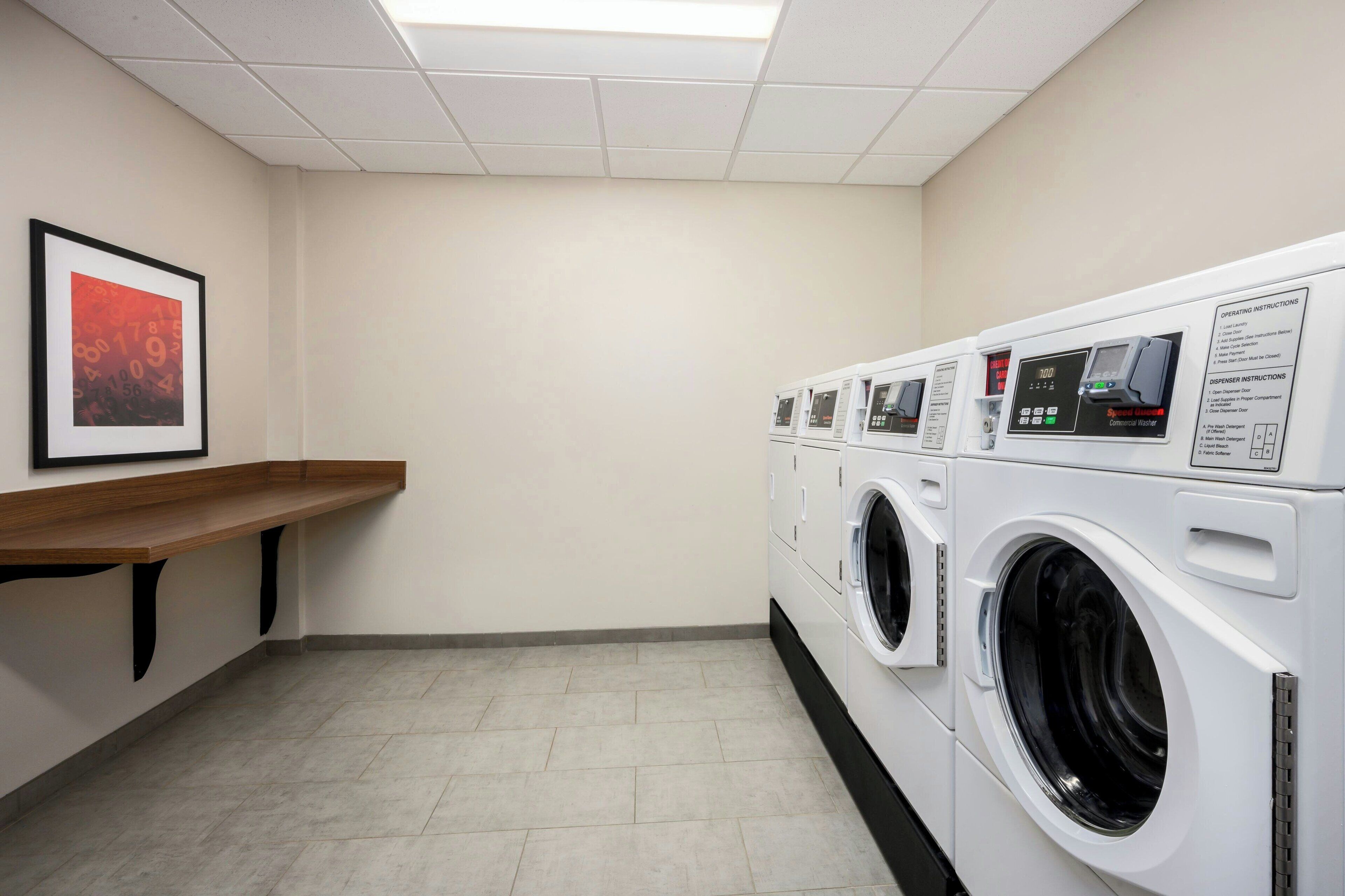 A laundry room with a bench, multiple washing machines, and operating instructions.
