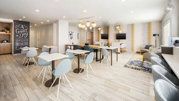 A modern dining area with multiple tables and chairs, a kitchen area with a chalkboard sign, and a seating area with sofas and a TV.