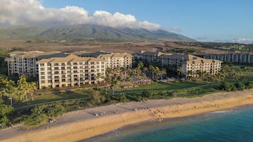 Un resort con varias construcciones, una playa y montañas al fondo.