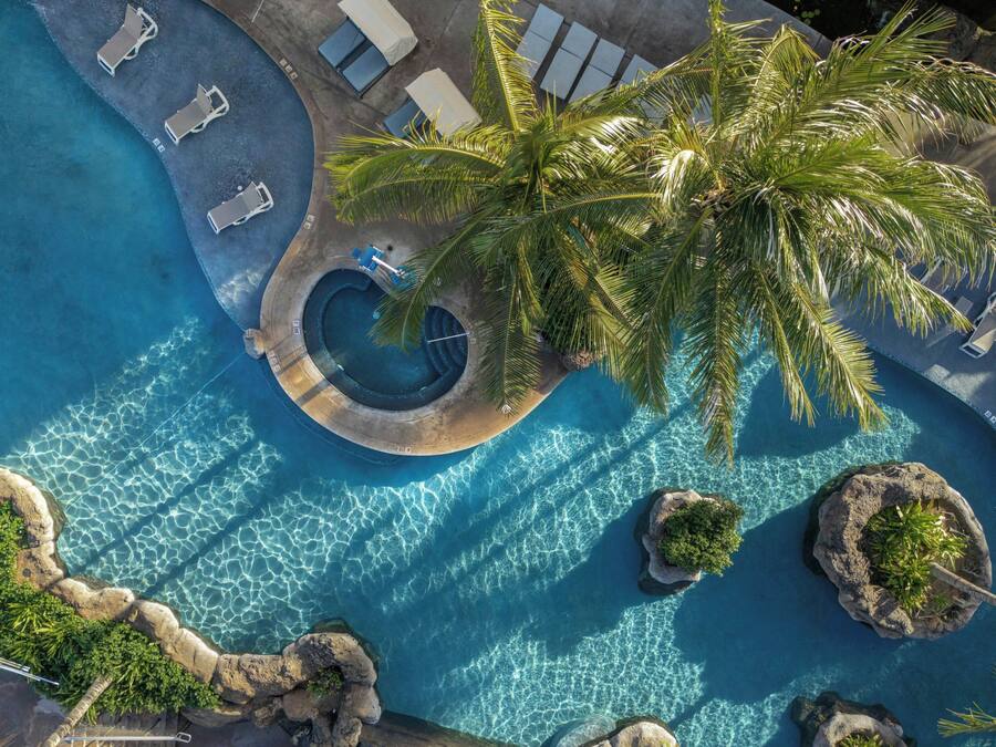 Eine Luftaufnahme eines Resort-Poolbereichs mit Whirlpool, Liegestühlen und Palmen.