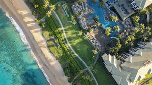 An aerial view of a resort with a beach, a swimming pool, and palm trees.