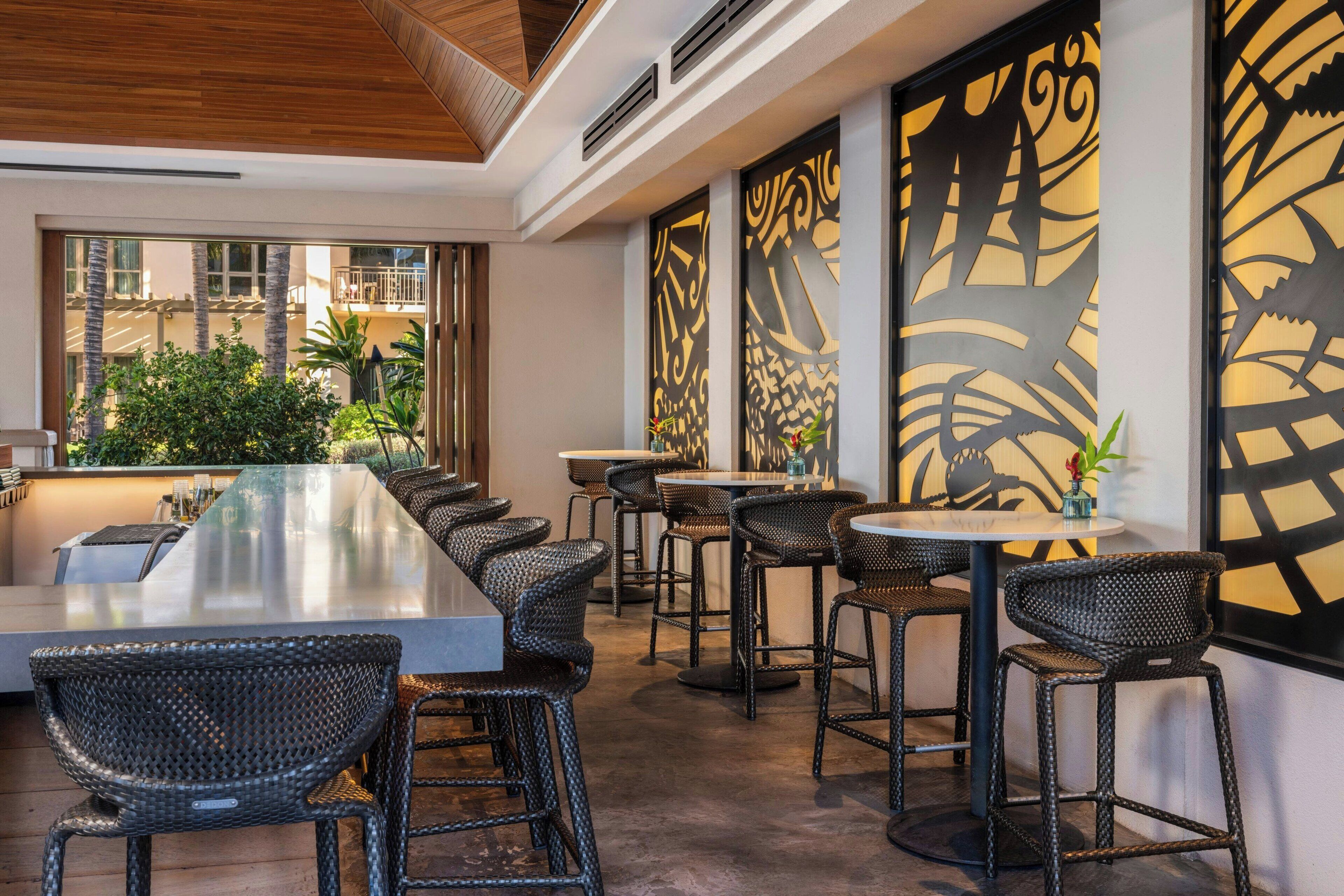 Un área de bar moderna con una barra alargada, sillas de mimbre y paneles decorativos en la pared.