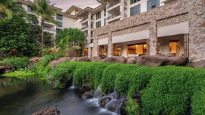 A hotel with a stone facade, a pool with a waterfall, and lush greenery.
