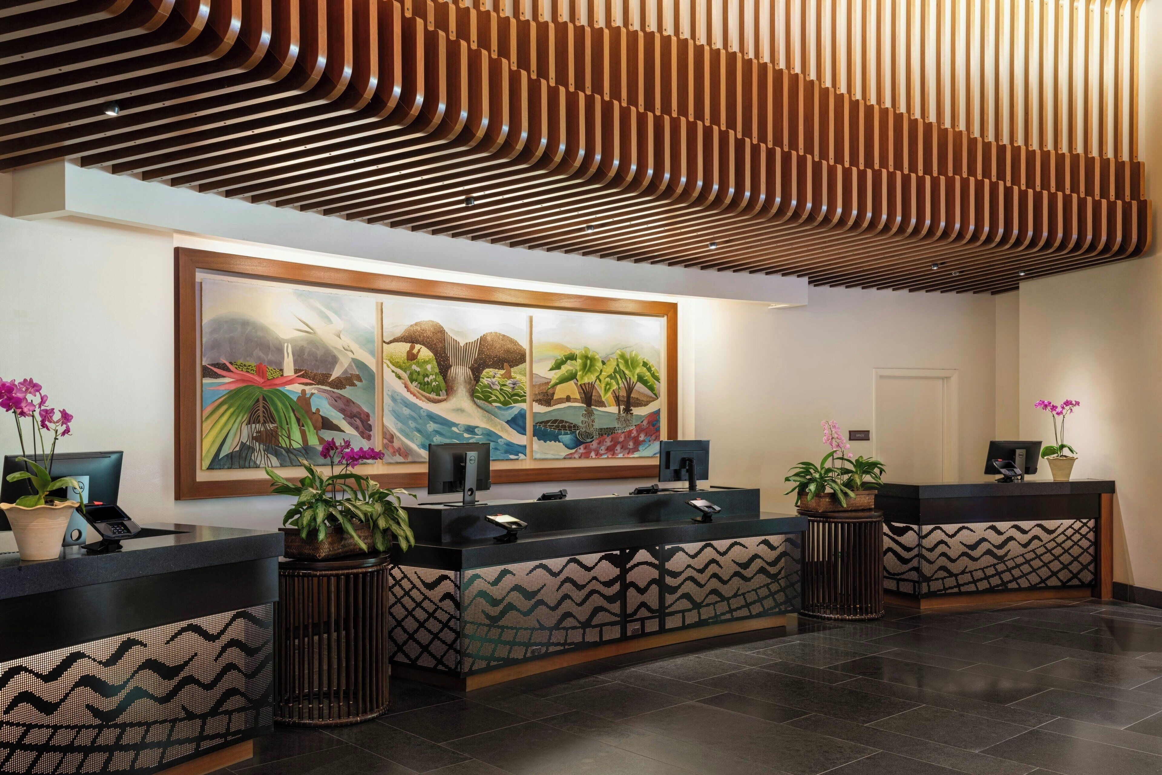 Un área de recepción con diseño moderno, que incluye un cuadro grande, mostradores de recepción y plantas en macetas.